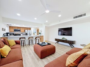 Ein modernes Wohnzimmer mit einer Couch, Hocker und einem an der Wand befestigten Fernseher.