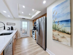 A modern kitchen with a stainless steel refrigerator, wooden cabinets, and a large painting of a beach scene. - Recently renovated BEACH condo, tons of amenities (Indian Shores)