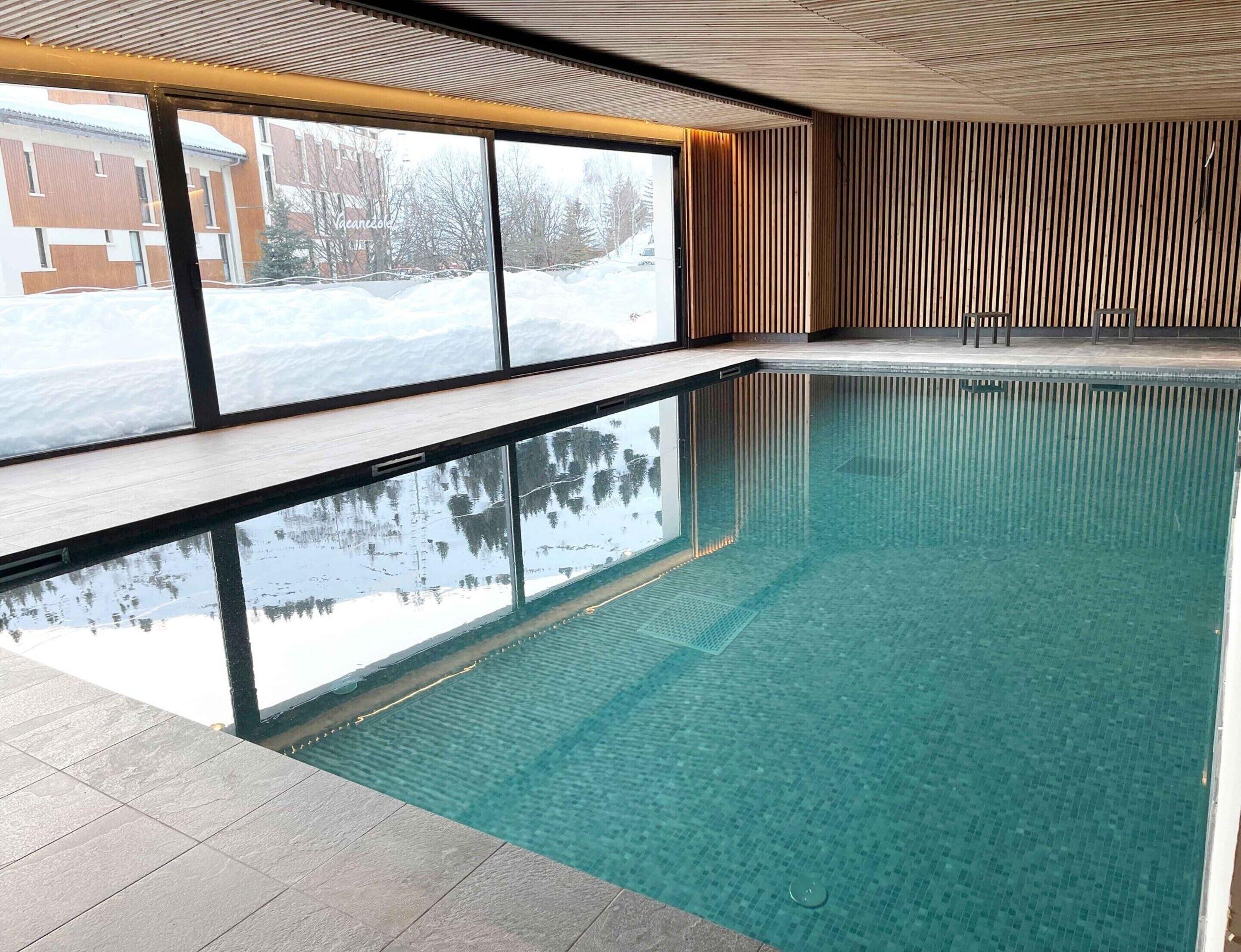 Une piscine intérieure aux eaux cristallines, offrant une vue sur un paysage enneigé grâce à de grandes fenêtres.