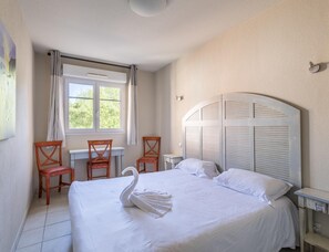 Ein Schlafzimmer mit einem Bett, zwei Stühlen, einem Schreibtisch, einem Fenster und einem Kopfteil.
