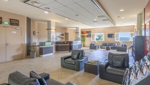 Een hotel lobby met een receptiebalie, een zithoek en uitzicht op het buitengebied.