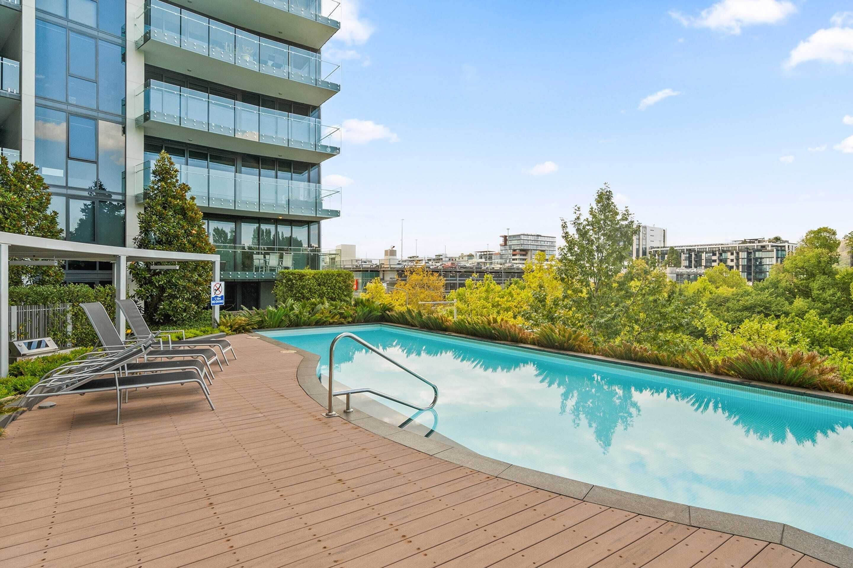 A modern building with a swimming pool, lounge chairs, and a clear view of the city skyline.