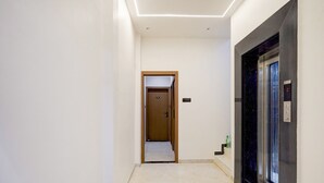 A hallway with a marble floor, a wooden door, and an elevator.