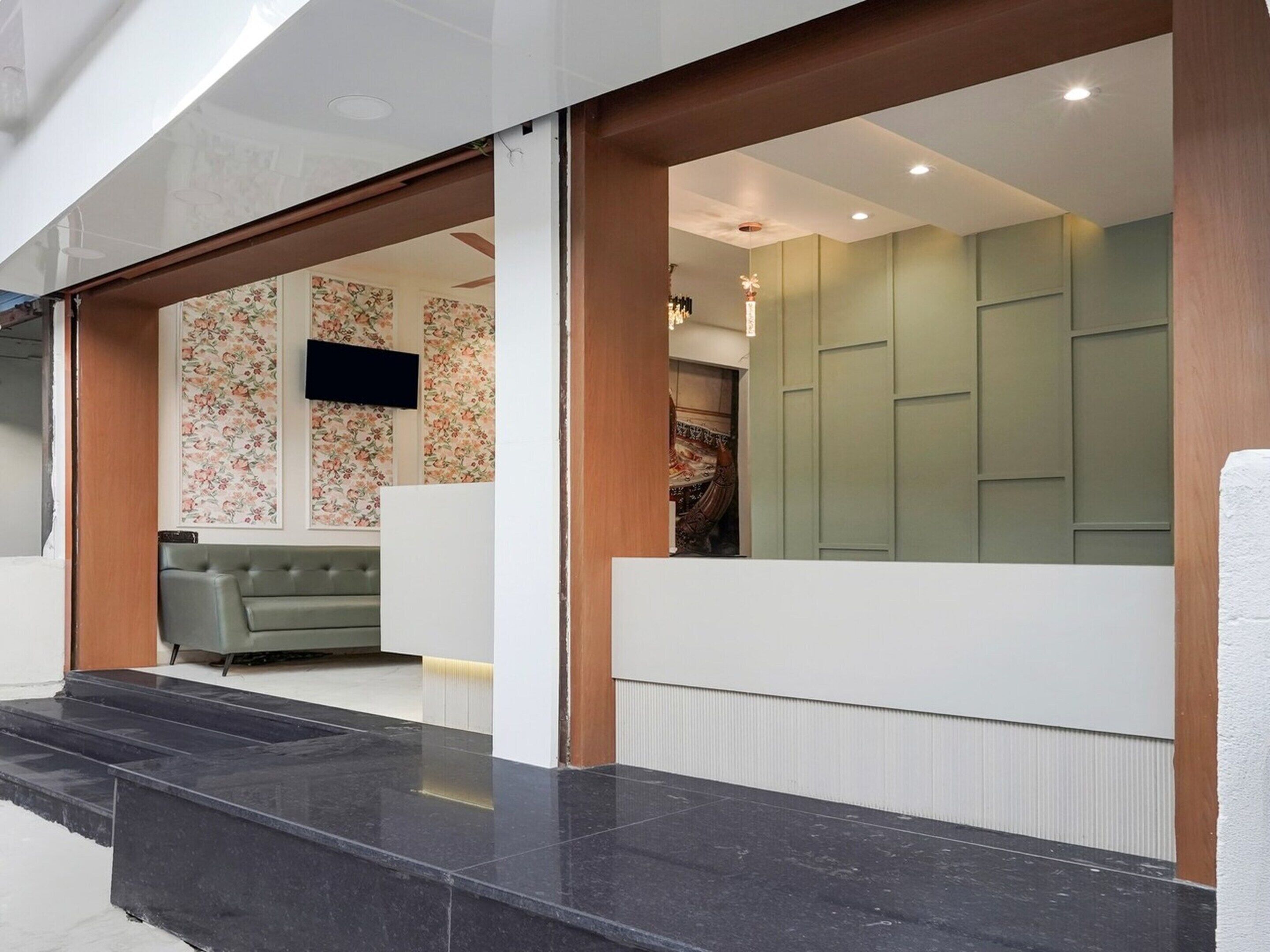 A reception area with a grey sofa, a flat-screen TV, and a green wall with patterned wallpaper.