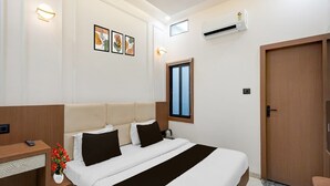 A hotel room with a bed, bedside table, lamp, air conditioning unit, and a window.