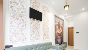 A modern interior with a light blue sofa, floral wallpaper, a mounted TV, and a large decorative painting.