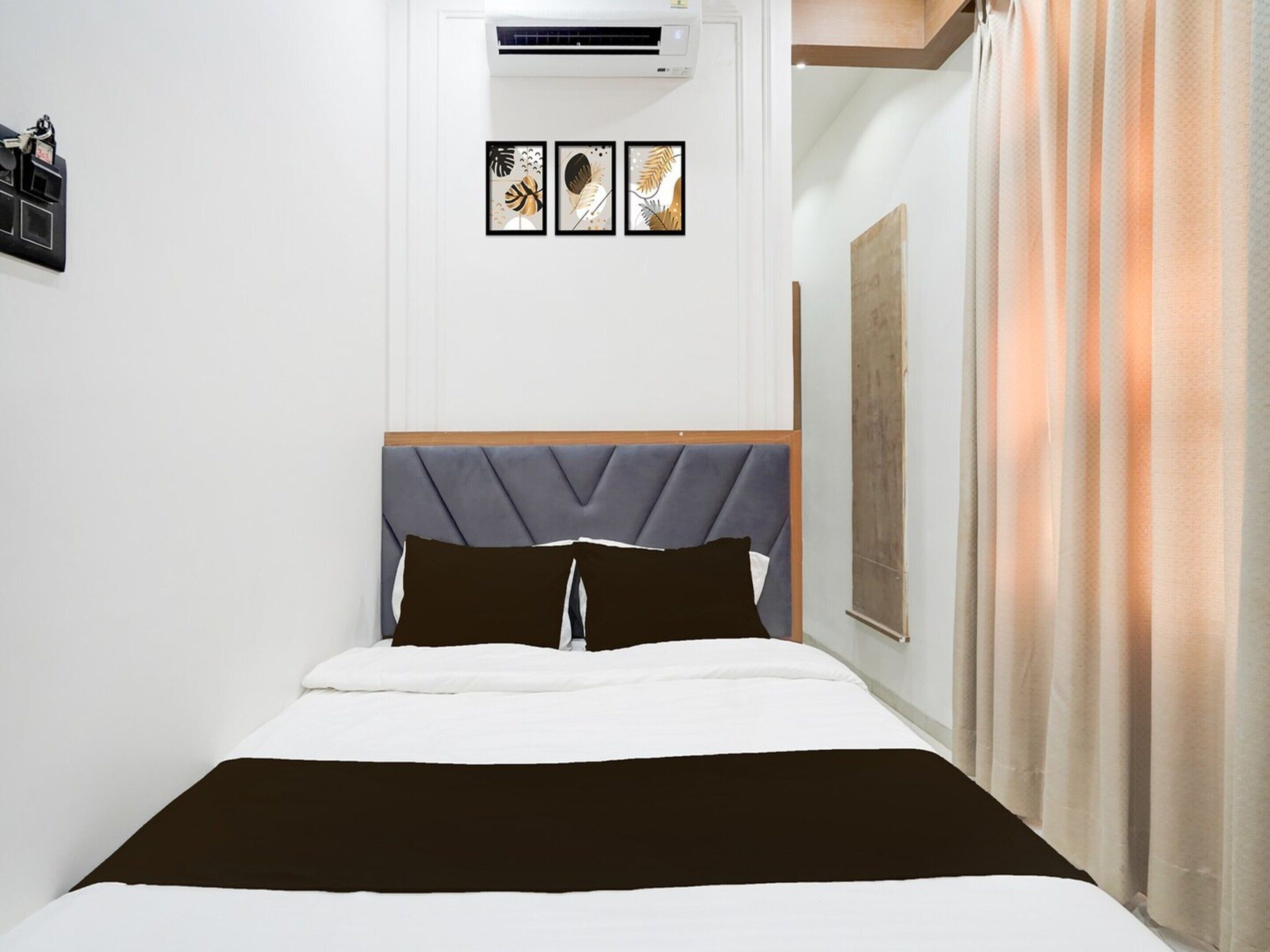 Quarto com cama, cabeceira, ar condicionado fixado na parede e quadros emoldurados.