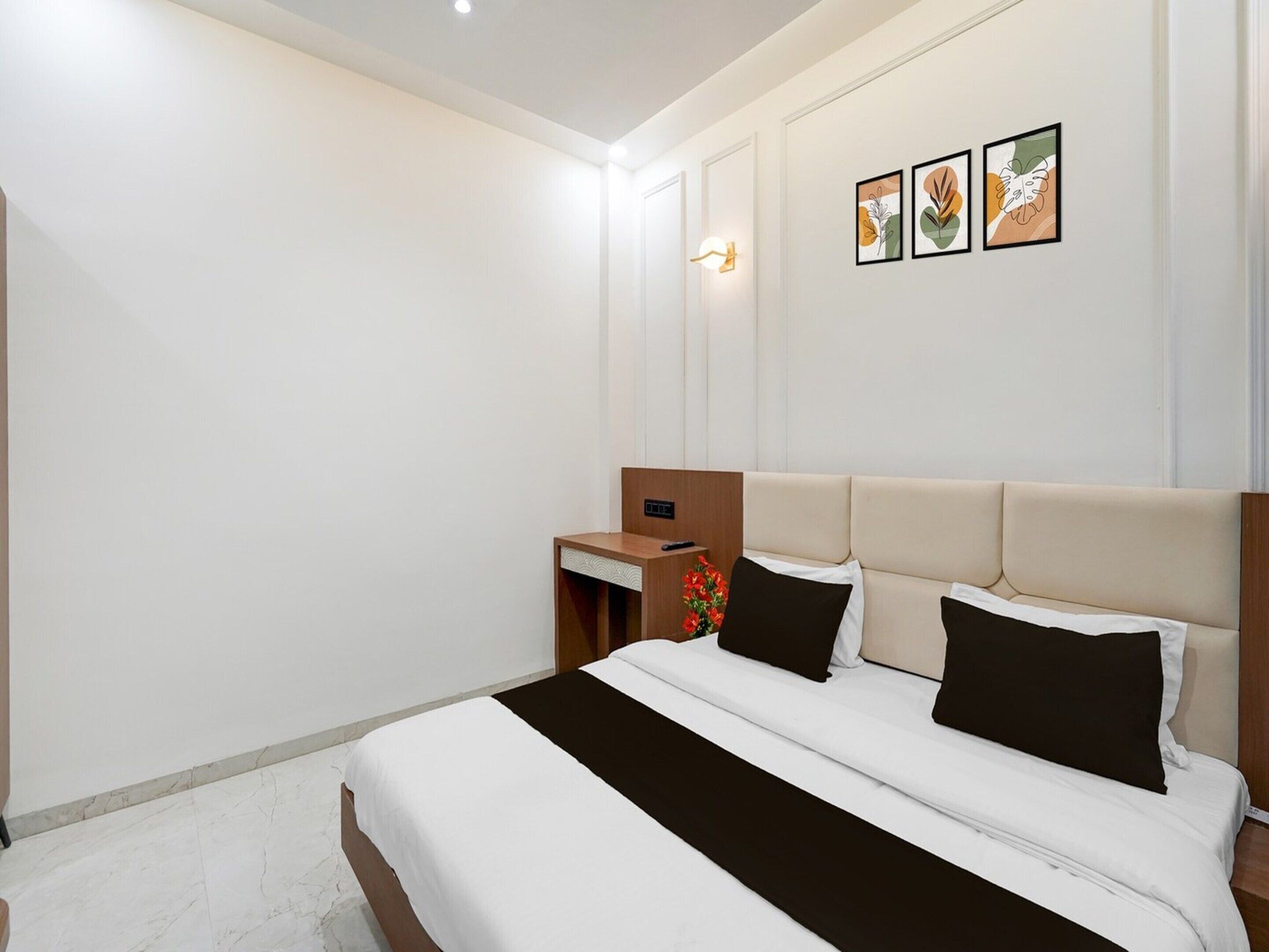 Una habitación de hotel con una cama, una mesita de noche, una lámpara de pared y tres obras de arte enmarcadas.