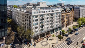 Un edificio de varios pisos con fachada moderna de vidrio, un patio con asientos y una línea de tranvía.