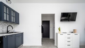 Una cocina moderna con armarios oscuros, encimera de mármol y un mueble de almacenaje blanco con cajones.