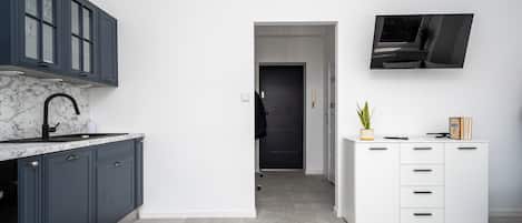 A modern kitchen with dark cabinets, a marble countertop, and a white storage unit with drawers.