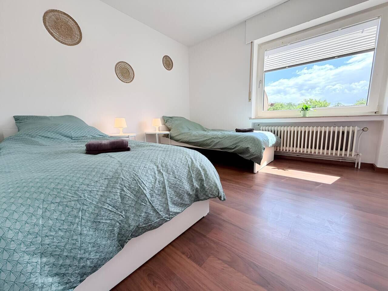 Un dormitorio con dos camas, un radiador, una ventana con vistas y decoración en las paredes.