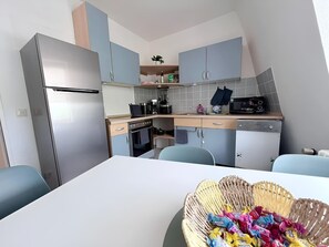Eine kleine Küche mit Kühlschrank, Herd und Mikrowelle. Ein Esstisch mit einer Leckerei-Auswahl steht bereit.