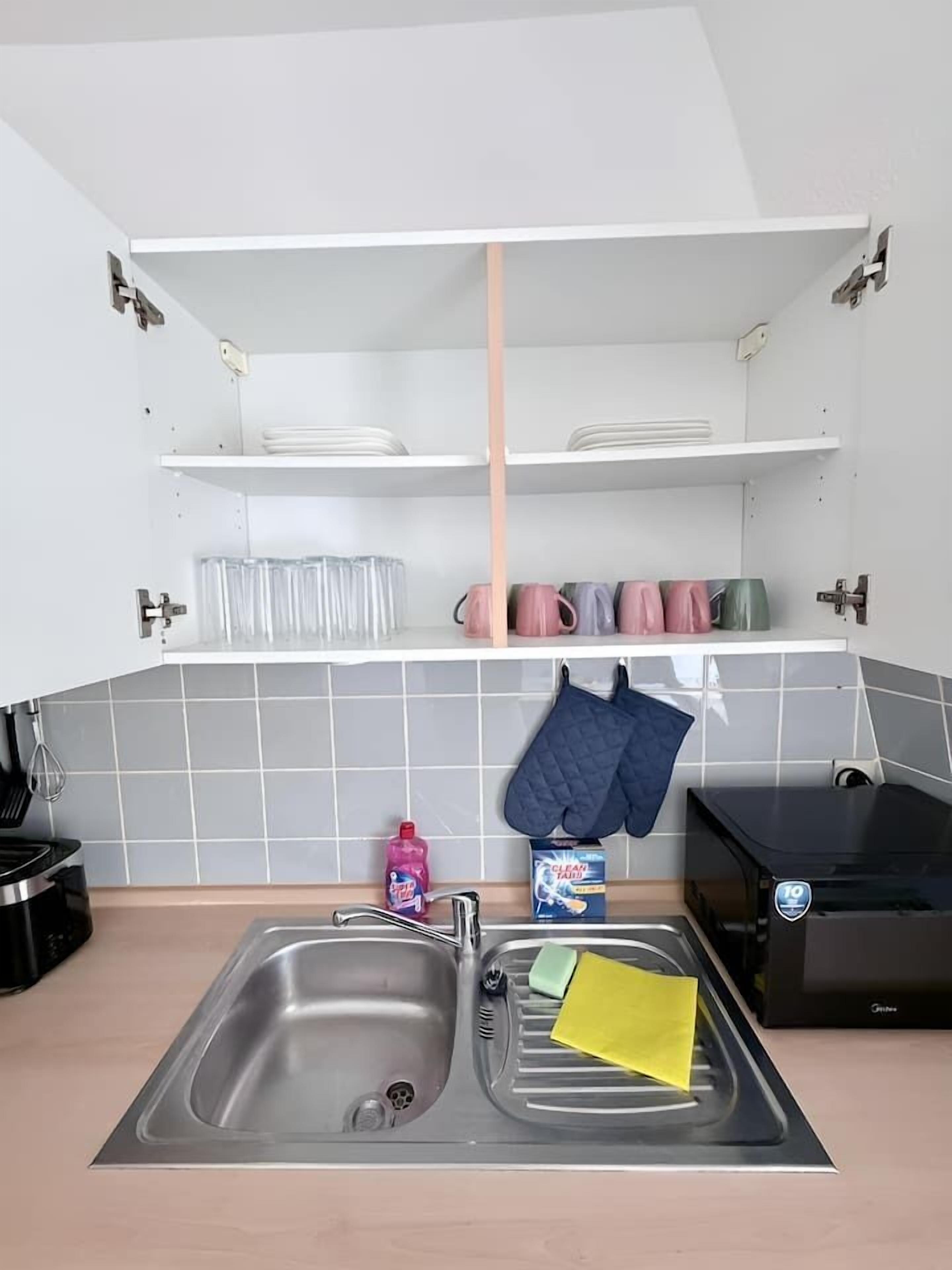 Eine Küche mit doppelter Spüle, einer Mikrowelle, einem Toaster und einem Regal über der Spüle mit Tellern und Tassen.