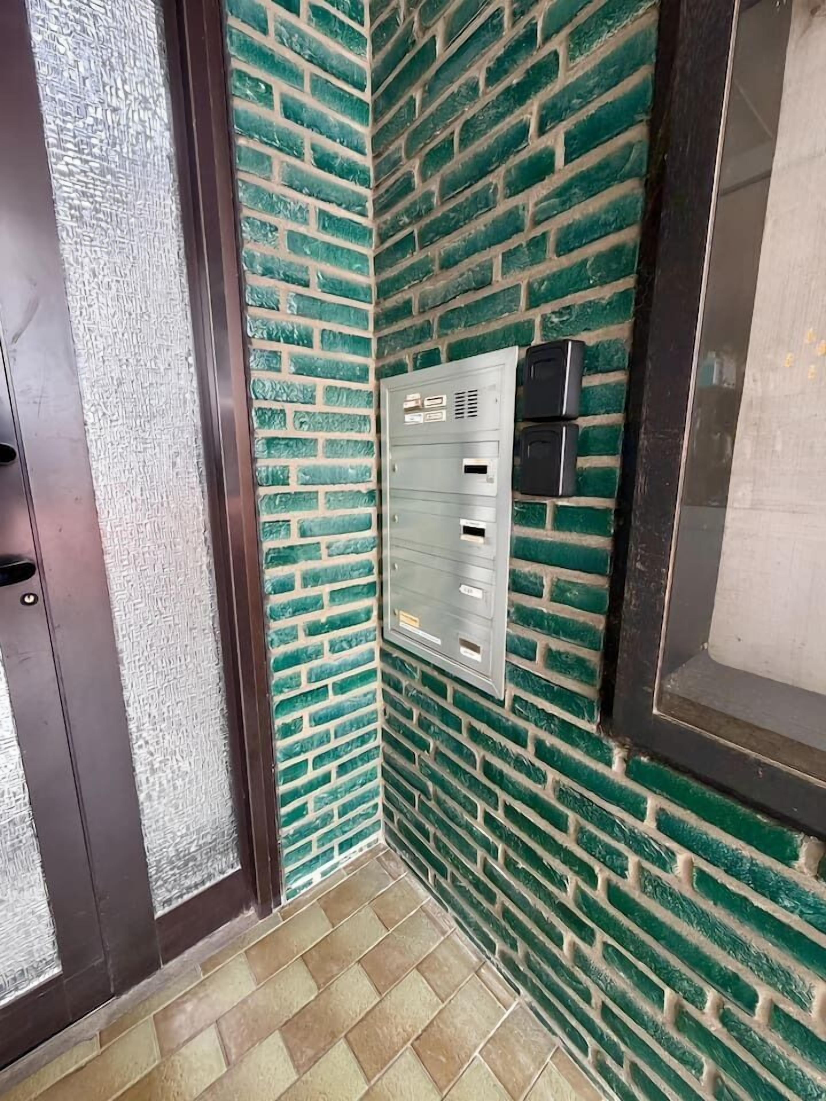 Un angolo di una stanza con una parete in mattoni verdi, un quadro elettrico in metallo e una porta.