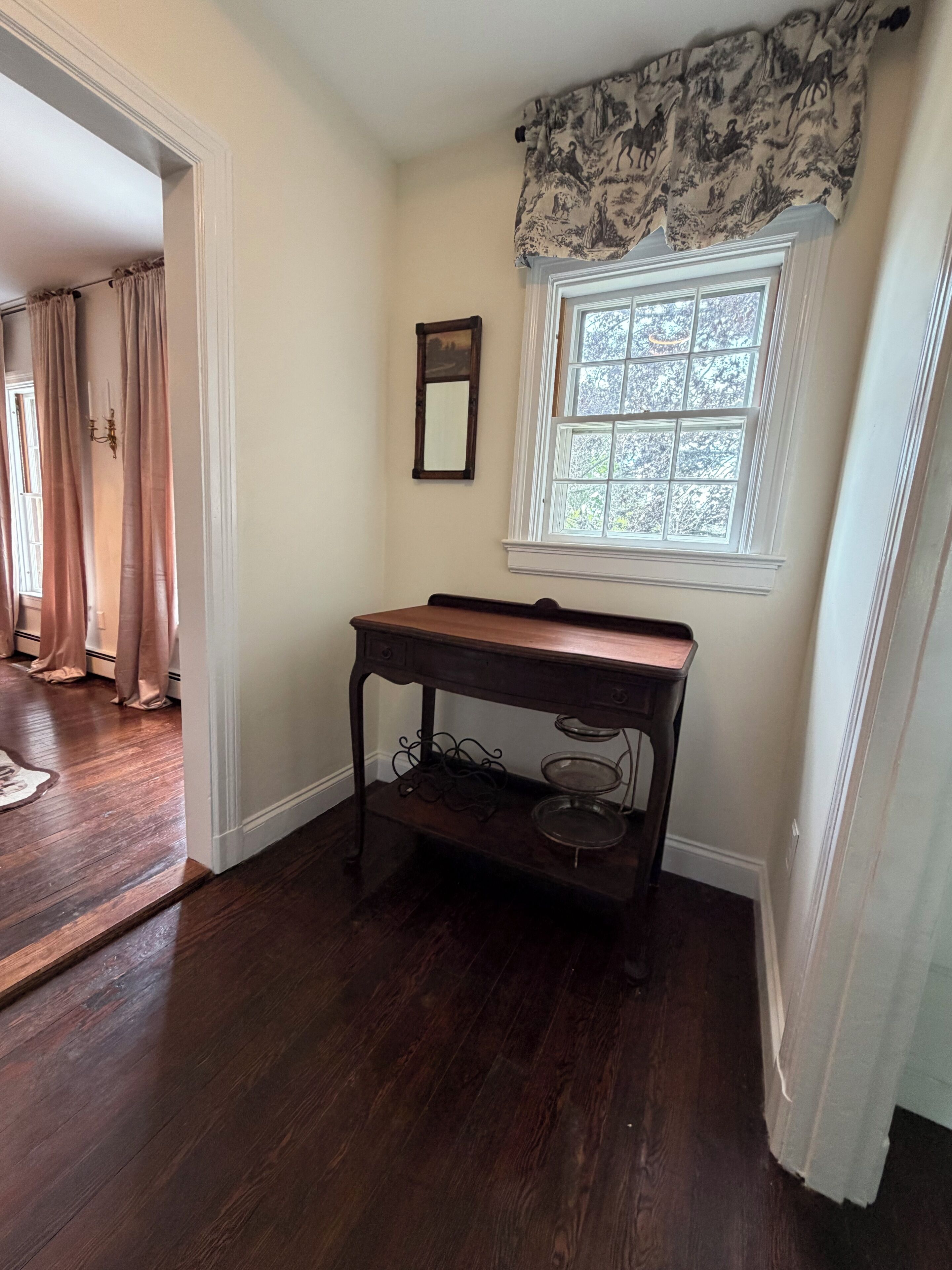 Quarto com escrivaninha de madeira, janela com vista, espelho e lustre.