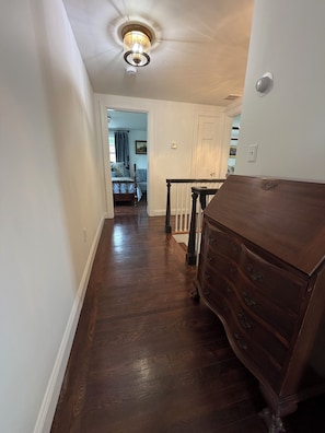 A hallway with a wooden dresser, a staircase, and a door leading to a bedroom. - Fabulous 4 bedroom 4 bath home in charming Portsmouth RI Steps from Newport Polo (Portsmouth)
