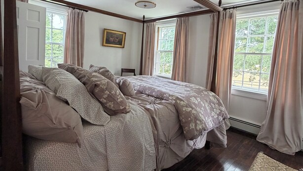 Una camera da letto con un letto grande, travi in legno, ventilatore a soffitto e finestre con tende.