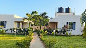 A modern building with a central pathway, surrounded by lush greenery and palm trees. - Le Grande Haven Shimoni (Kanana)