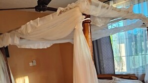 A wooden four-poster bed with a canopy, a ceiling fan, and a window with curtains. - Le Grande Haven Shimoni (Kanana)