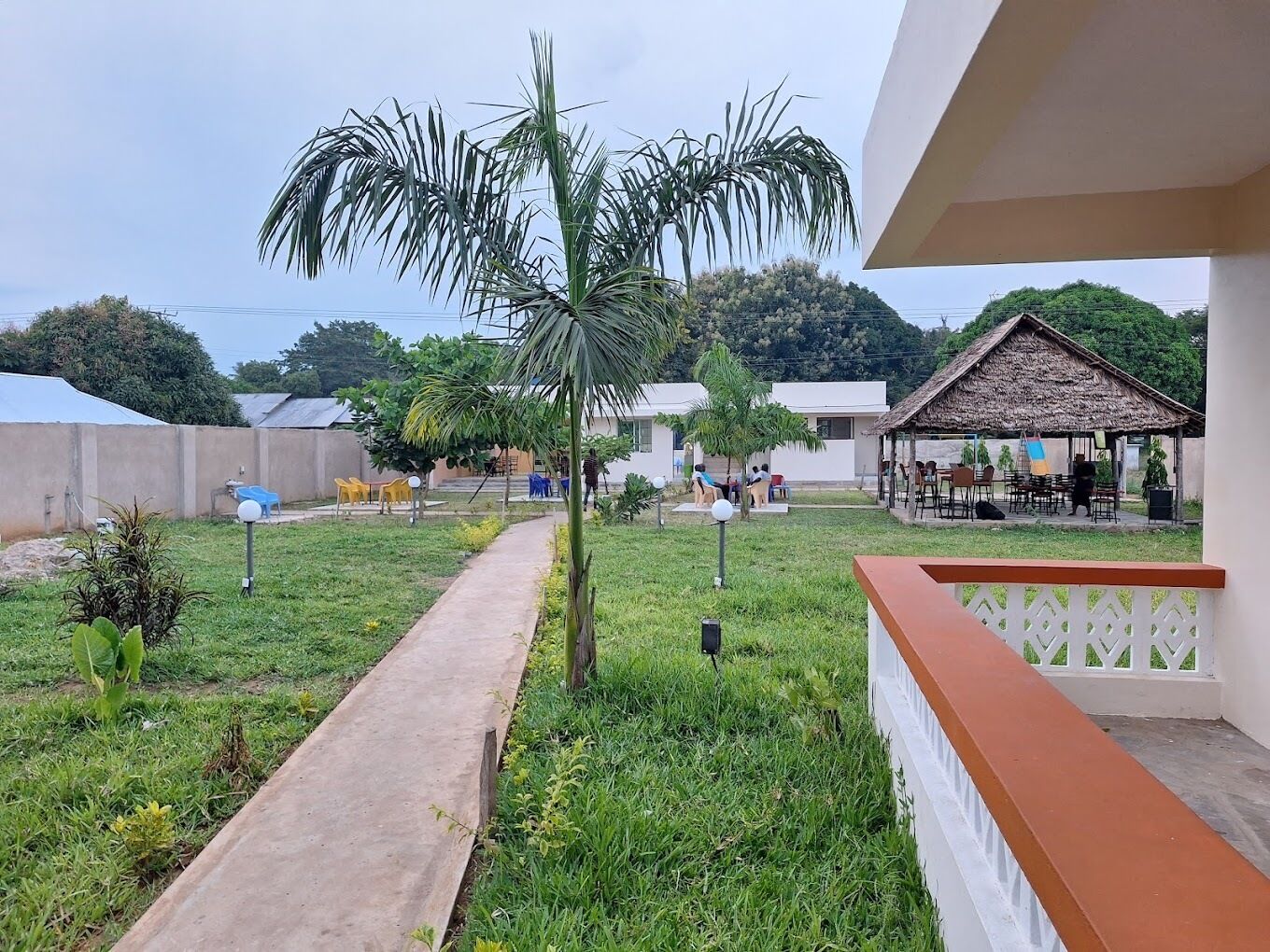 Un patio con un sendero de concreto, una palmera y una estructura con techo de paja.