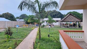 Un patio con un sendero de concreto, una palmera y una estructura con techo de paja.