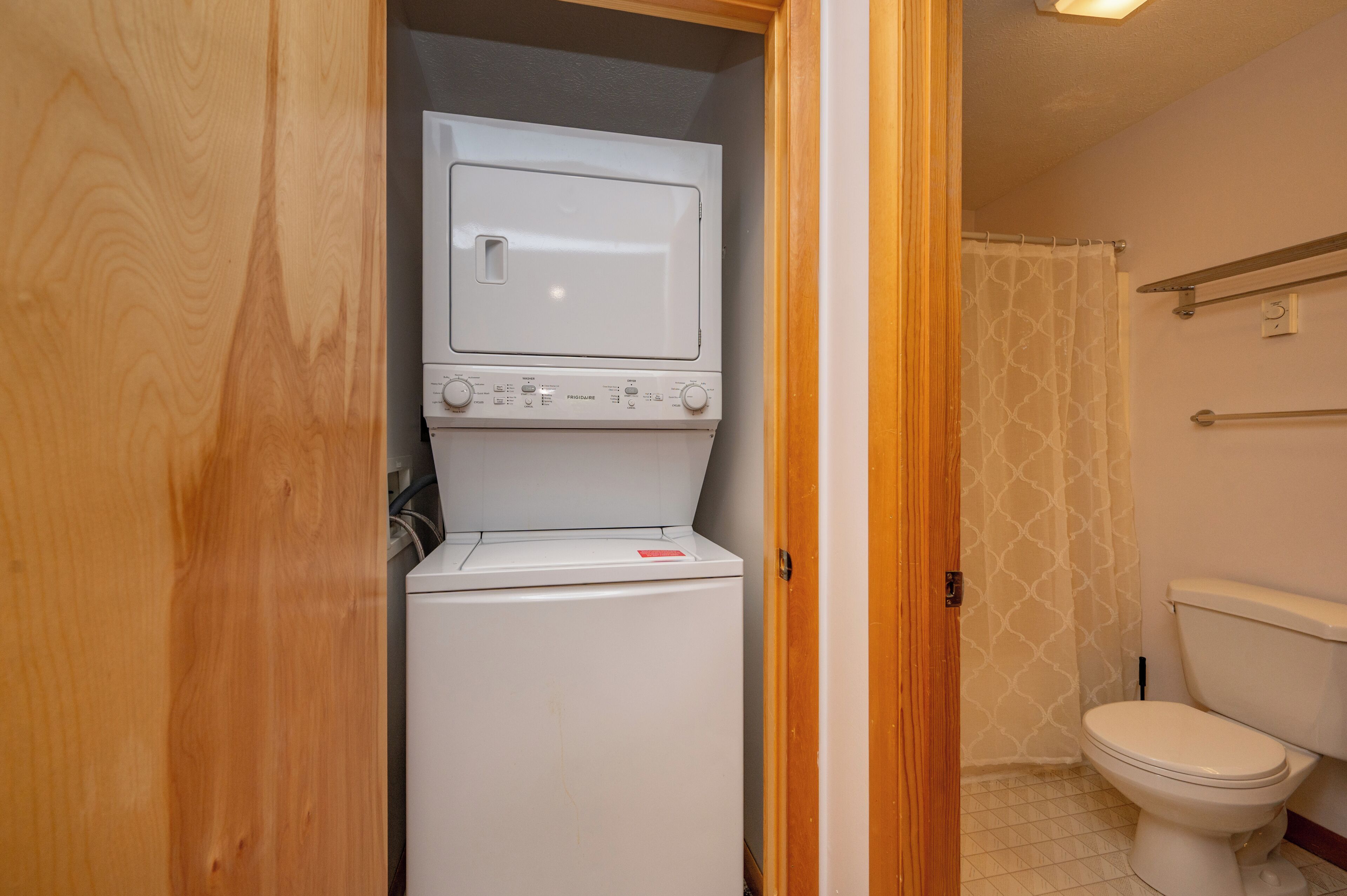 A compact laundry room with a washer and dryer, a toilet, and a shower curtain.