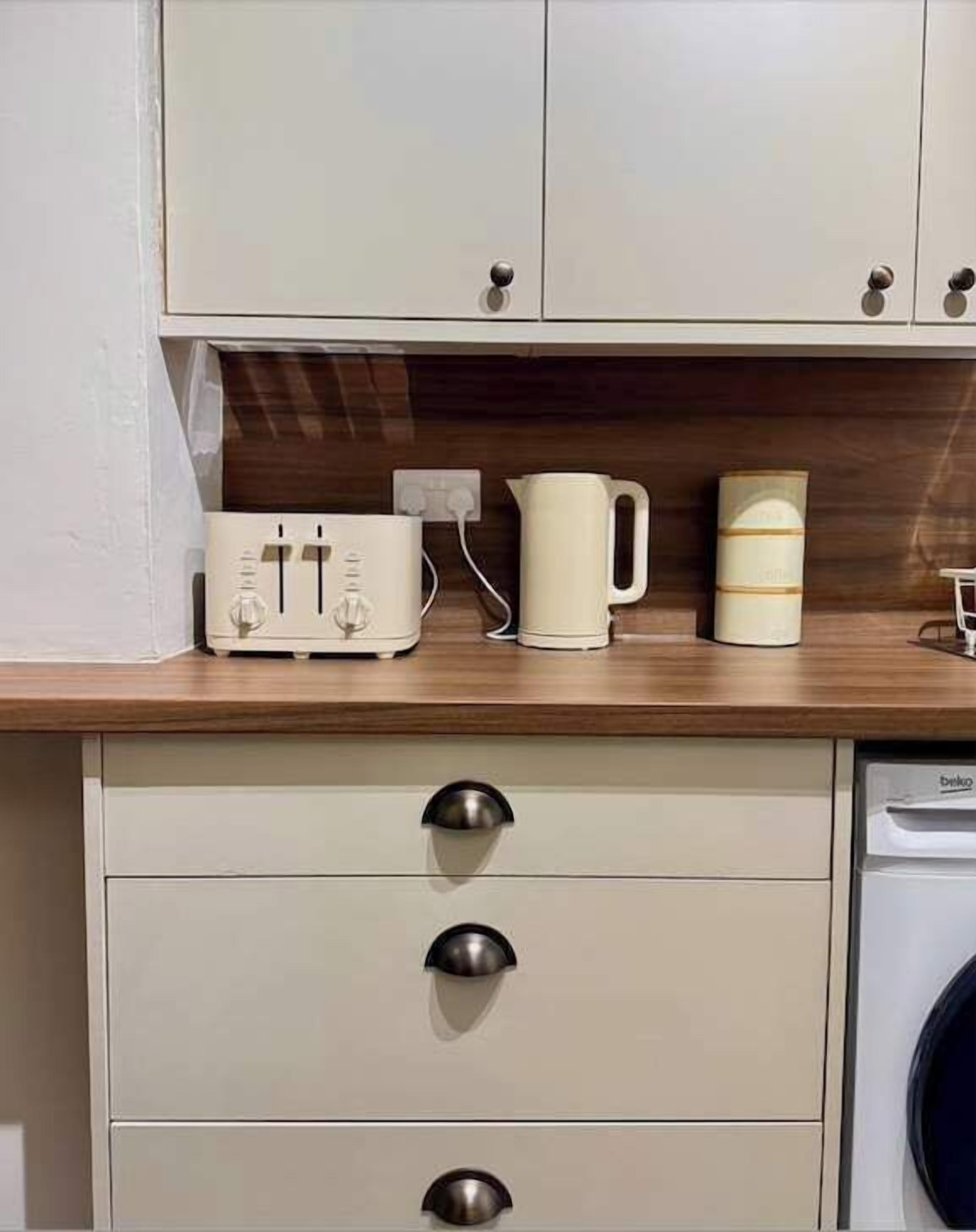 Een keuken met een houten aanrecht, een witte broodrooster, een witte waterkoker en een wasmachine.