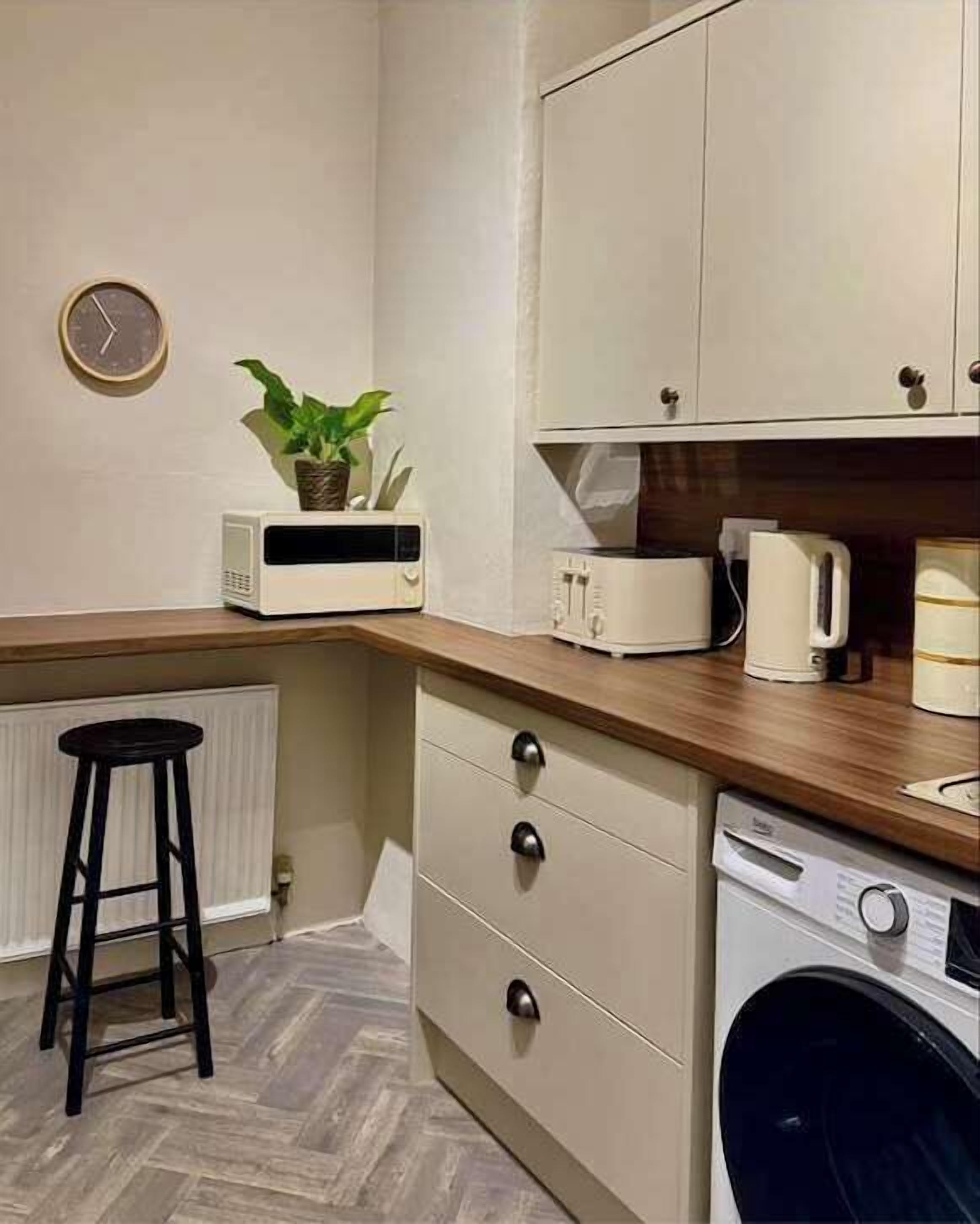 Une cuisine compacte équipée d’un lave-linge, d’un four à micro-ondes et d’une machine à café, le tout installé sur le plan de travail.