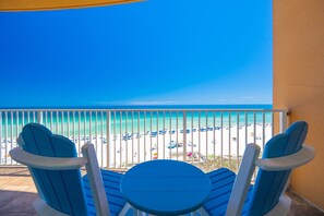 A balcony with two blue chairs and a small table, overlooking a beach with umbrellas and beach chairs. - Phoenix Orange Beach 505 3 Bedroom Condo (Orange Beach)