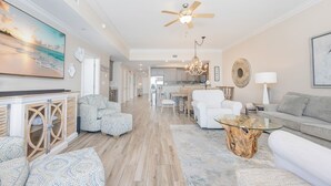 A spacious living area with a ceiling fan, a large painting, and a dining area in the background. - Phoenix Orange Beach 1902 3 Bedroom Condo (Orange Beach)