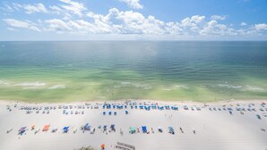 A beach with rows of sun umbrellas and beach chairs, a clear sky, and calm sea. - Phoenix Orange Beach 1902 3 Bedroom Condo (Orange Beach)
