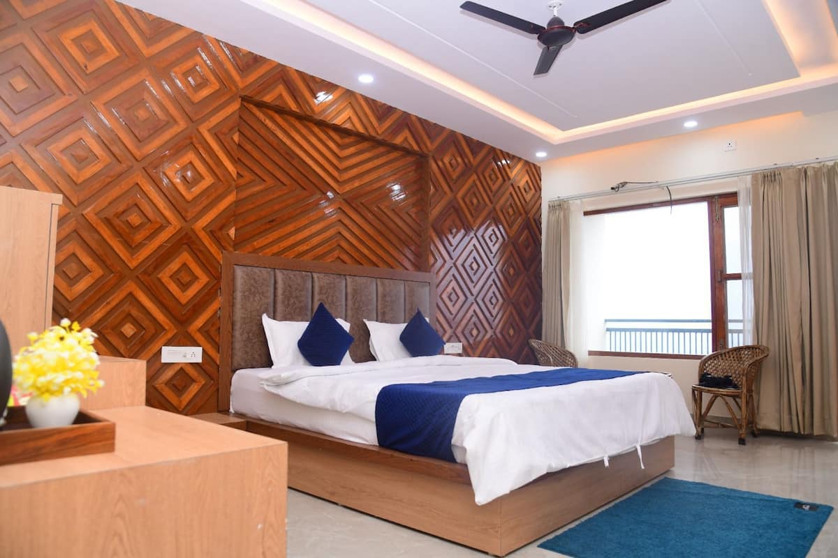 A hotel room with a bed, a desk, a chair, a ceiling fan, and a window with curtains.