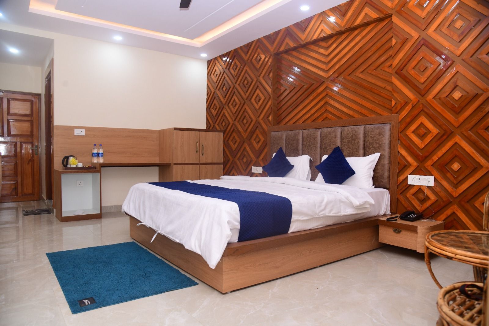 A hotel room with a bed, nightstand, wooden wardrobe, and a patterned wall.