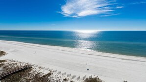 Ein Strand mit blauem Himmel, sandigem Ufer und einer Holzpromenade, die zum Wasser führt.