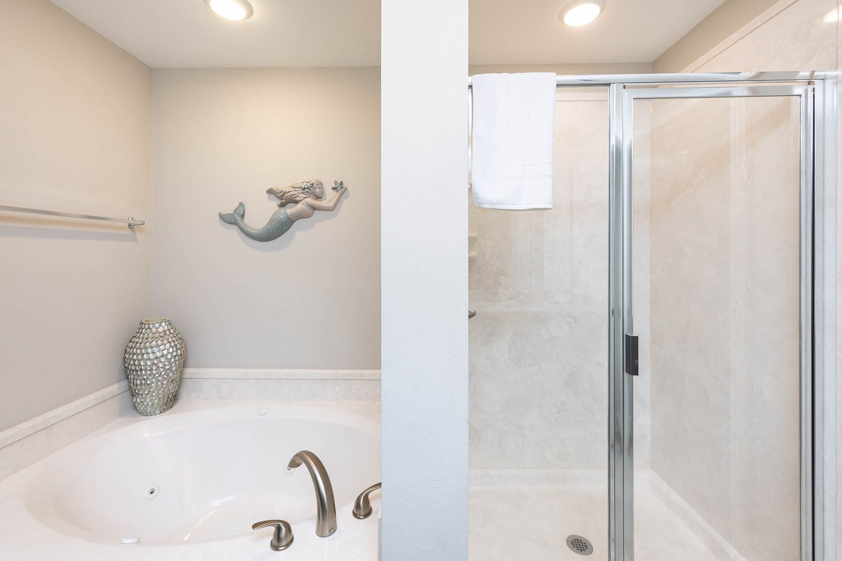 A bathroom with a bathtub, a shower, a decorative mermaid wall art, and a decorative vase.