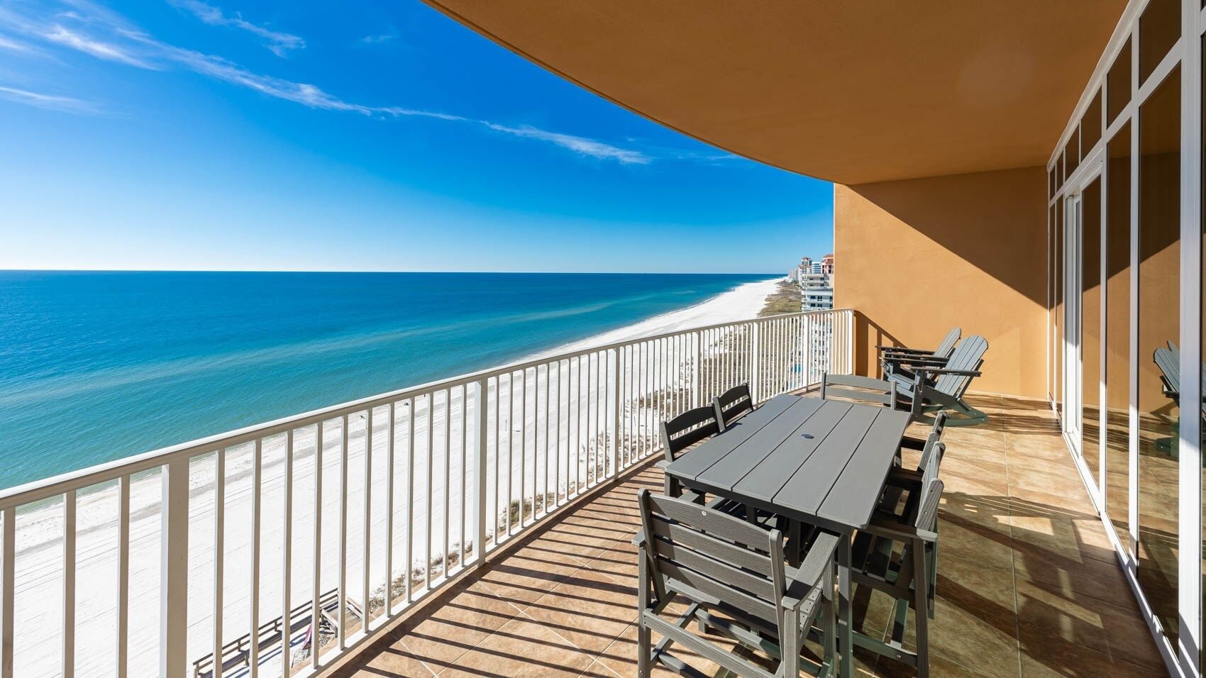 A balcony with a view of the ocean, a wooden deck, and a table with chairs.