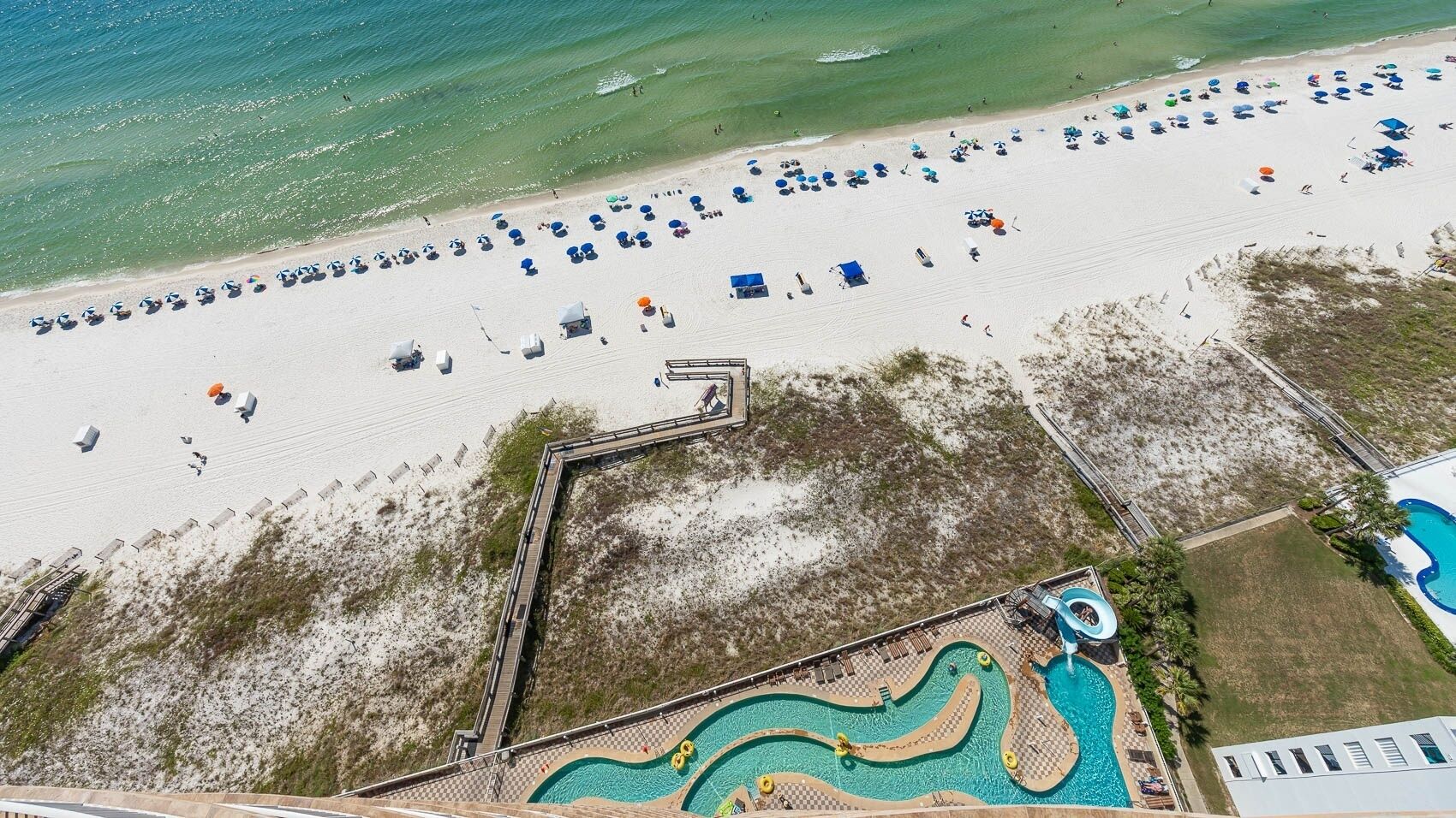 An aerial view of a beach resort with a swimming pool, beach umbrellas, and a sandy shoreline.