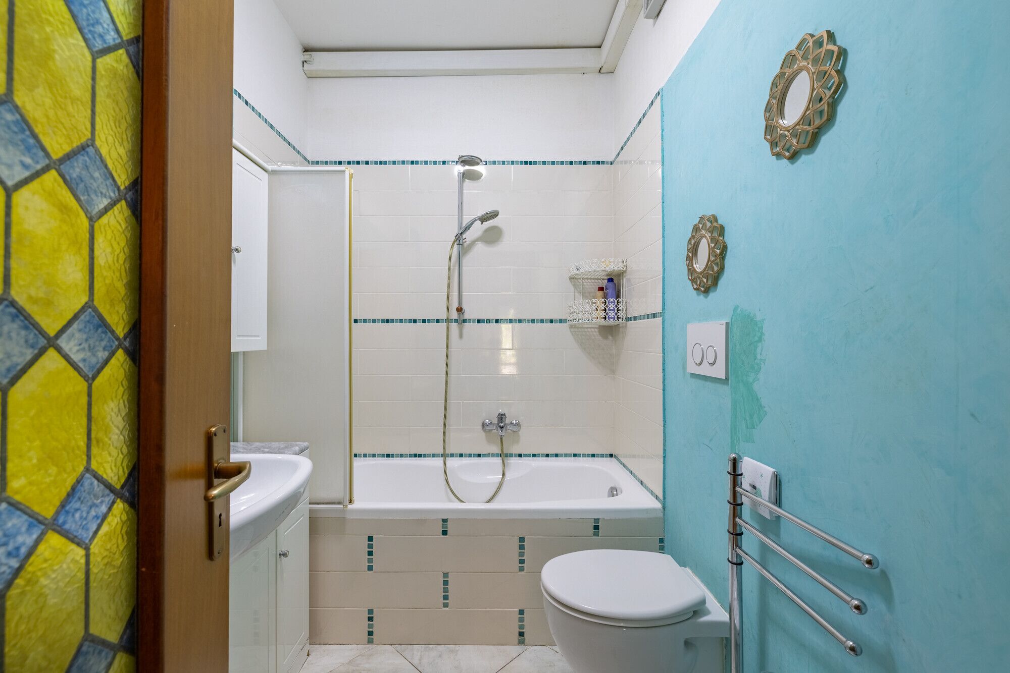 Ein Badezimmer mit Dusche, Toilette und Waschbecken, mit blauer Wand und gefliestem Boden.
