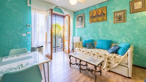 A room with teal walls, a ceiling fan, a sofa with blue cushions, a table with a glass top, and artwork on the walls. - Il Giardino by Wonderful Italy (Sanremo)