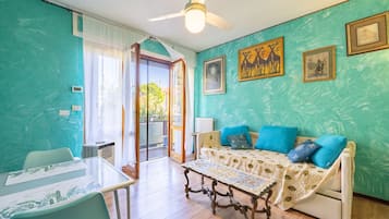 Una stanza con pareti color acquamarina, una ventola a soffitto, un divano con cuscini blu, un tavolo con piano in vetro e opere d'arte alle pareti.