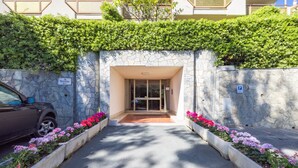 A hotel entrance with a stone facade, a car parked outside, and flower beds on either side. - Il Giardino by Wonderful Italy (Sanremo)