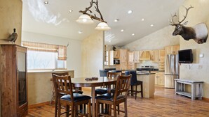 Una cocina amplia con armarios de madera, un comedor con una mesa grande y sillas, y una cornamenta de alce montada en la pared.