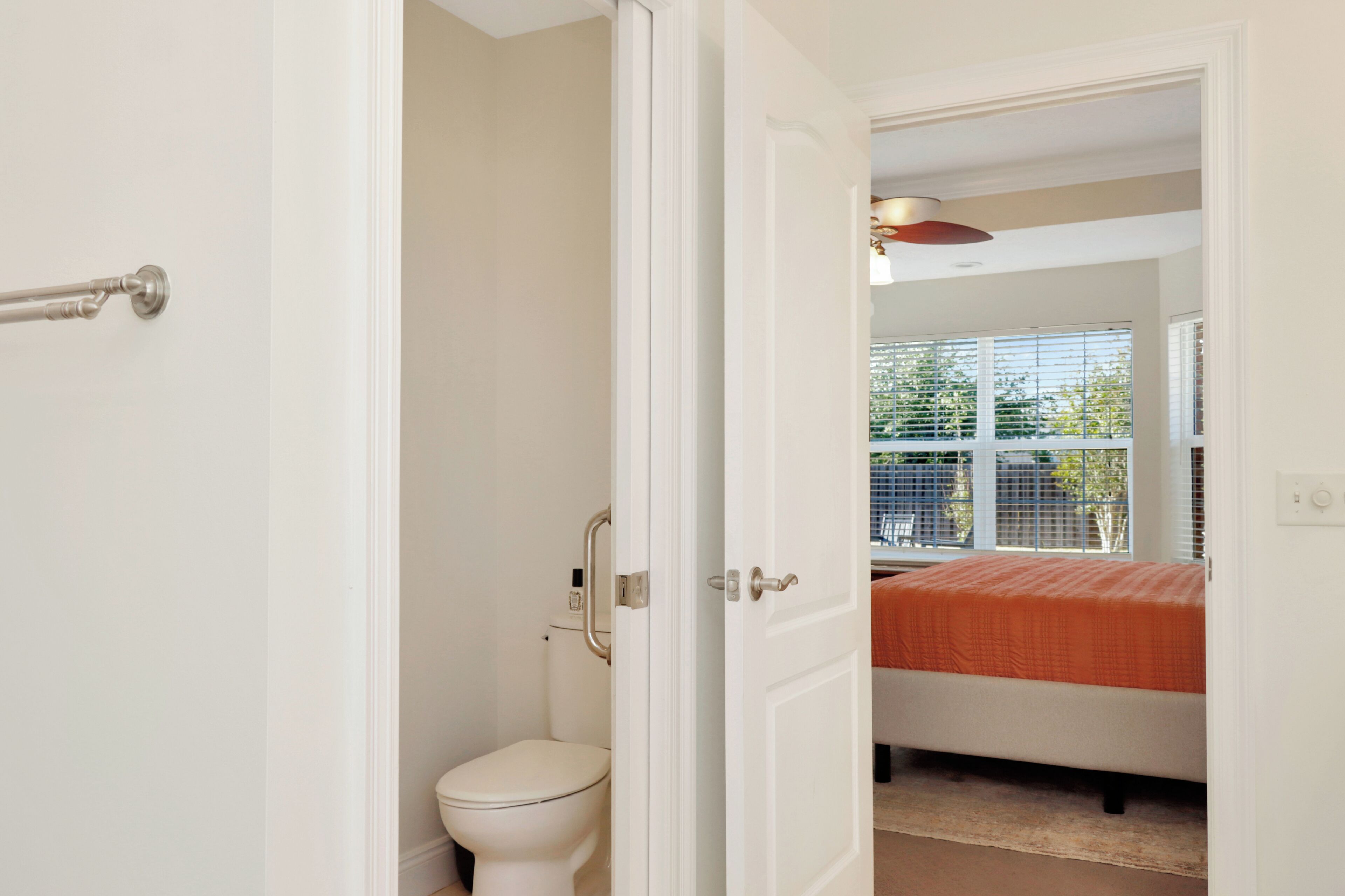 Une pièce avec un lit, une fenêtre avec des stores, des toilettes et une porte.