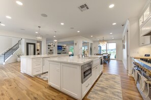 A spacious kitchen with white cabinetry, a large island, and a dining area with a view. - Villa de Lago! A Stunning Waterfront Estate on Lake Conroe (Montgomery)