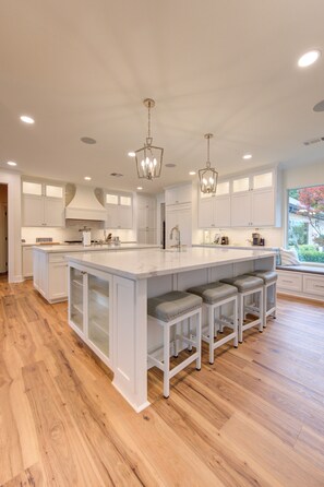 A modern kitchen with a large island, white cabinetry, and wooden flooring. - Villa de Lago! A Stunning Waterfront Estate on Lake Conroe (Montgomery)