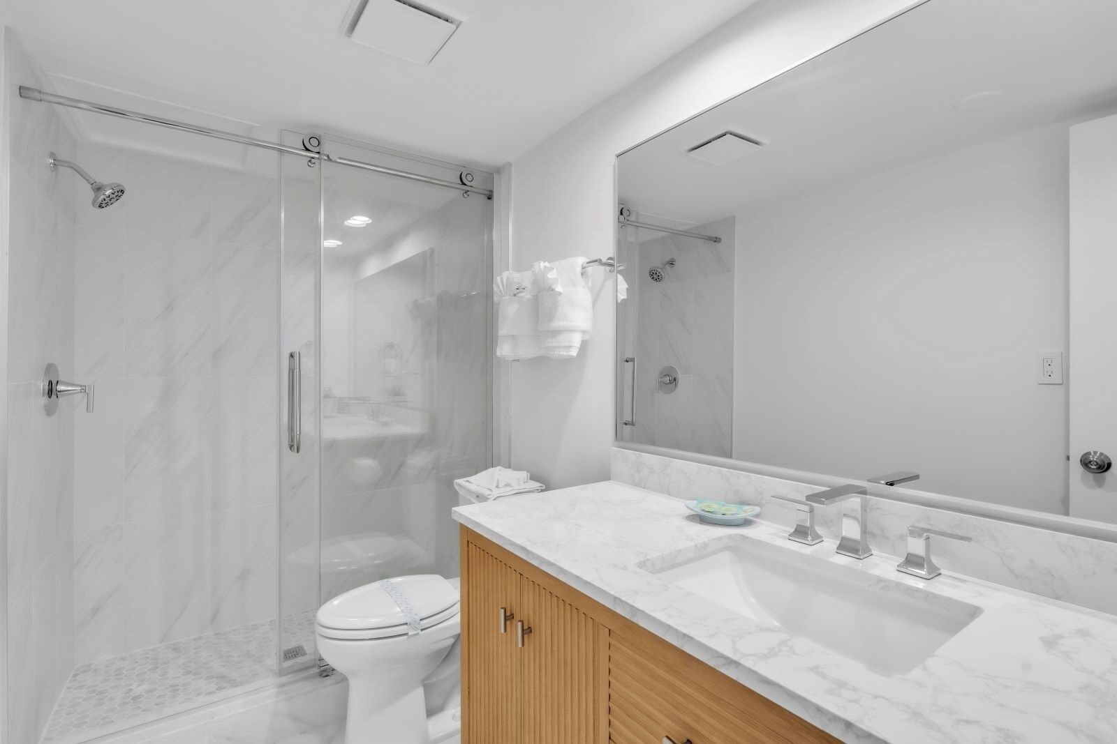 A modern bathroom with a glass shower enclosure, a white toilet, a marble sink, and wooden cabinets.