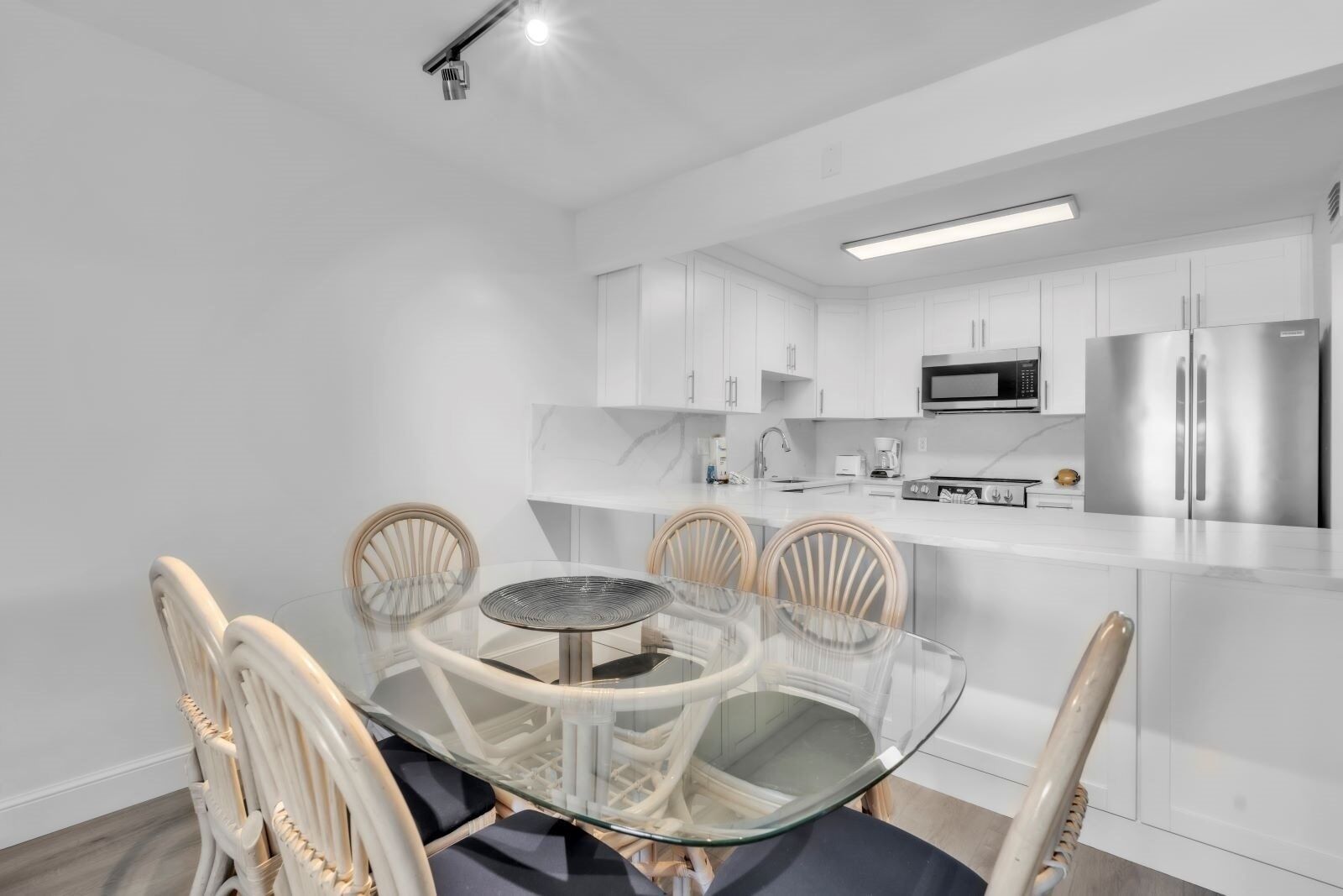 A modern kitchen with white cabinets, stainless steel appliances, and a glass dining table with chairs.
