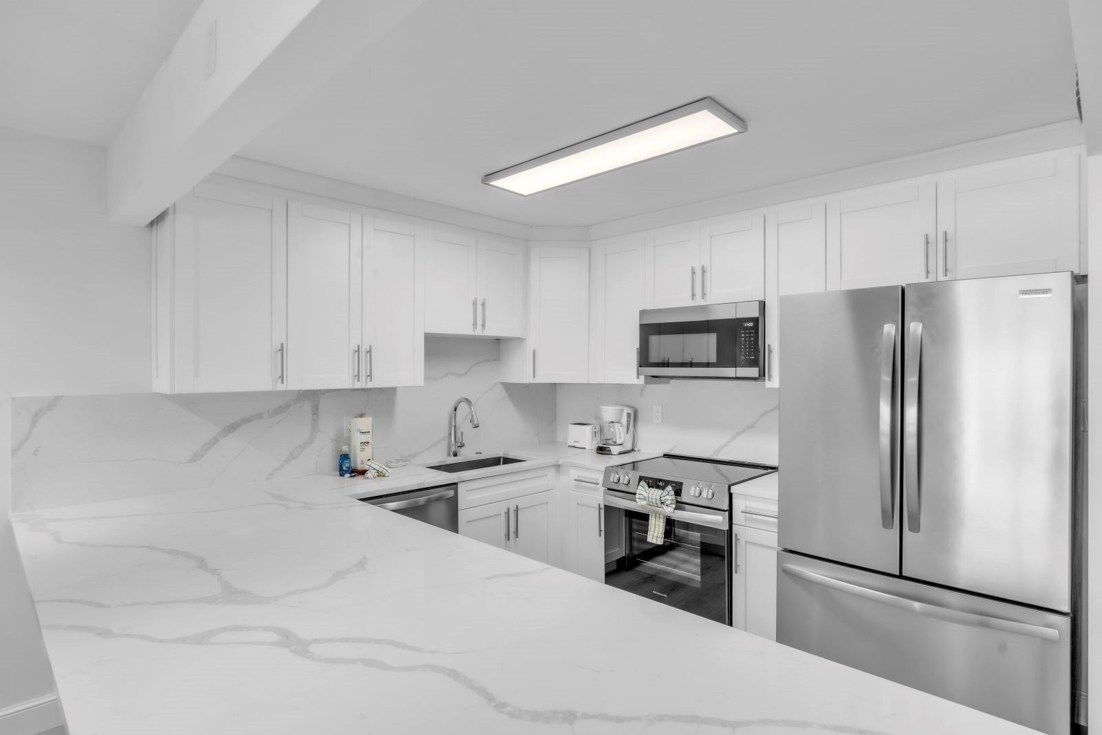 A modern kitchen with white cabinetry, a stainless steel refrigerator, a microwave, and a built-in oven.