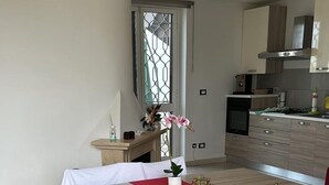 A dining area with a table and chairs, a window with a view, and a kitchen in the background. - Bright & Peaceful 2BR Apartment in Terracina (Terracina)